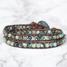 Genuine leather and African Turquoise stones make up this gorgeous double wrap bracelet. Always a favorite of jewelry addicts and fashionistas alike. If you want color, start here first. Features a beautiful rustic copper, Greek made button closure. A Bluefish Classic! 4mm(.157") diameter African Turquoise gemstones Unique Greek made copper button with patina, about 16mm (5/8") in diameter Rust brown leather Signature Bluefish logo heart charm 34 - 39 cm/13.5 - 15.5" length 2 button loop adjustm Turquoise Wrap Bracelet, Logo Heart, Boho Wrap Bracelet, Double Wrap Bracelet, African Turquoise, Turquoise Stones, Boho Bracelets, Turquoise Gemstone, Leather Wraps