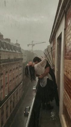 a man and woman kissing on top of a roof in the rain with buildings behind them