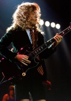 a man with long hair playing an electric guitar in front of spotlights on stage