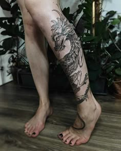 a man with a dragon tattoo on his leg is standing next to a potted plant