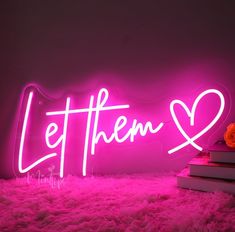 a pink neon sign that says let them love on top of a pile of books