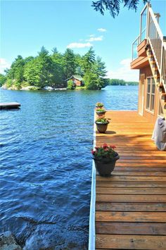 a wooden dock with potted plants on it next to a body of water and trees