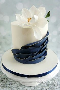 a white and blue wedding cake with a flower on top is featured in the instagram