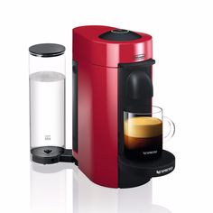 a red coffee maker with a cup next to it on a white surface and another machine in the background