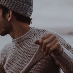 a man wearing a knitted hat and sweater holding a wooden stick in his hand