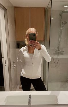 a woman taking a selfie in front of a bathroom mirror with her cell phone