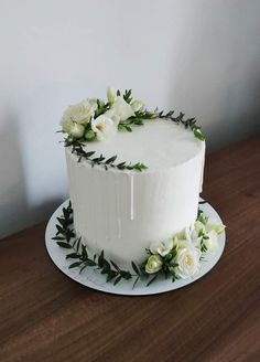 a white cake decorated with flowers and greenery on a wooden table top, ready to be eaten