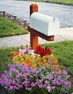 a mailbox sitting on top of a flower bed next to a sidewalk and street