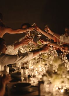 a group of people holding wine glasses in the air at a table with candles and flowers