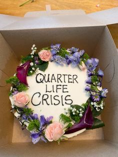 a cake in a box that says quarter life crisis on it with flowers around the edges