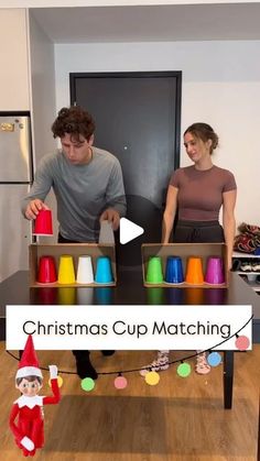 a man and woman standing in front of a christmas cup matching table with elf hats