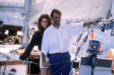 a man and woman standing on the deck of a sailboat