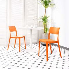 two orange chairs and a white table in a room with black and white tile flooring