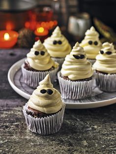 cupcakes with white frosting and black eyes on them sitting on a plate