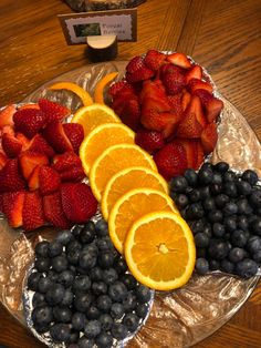 sliced oranges, blueberries and strawberries are arranged on a glass platter