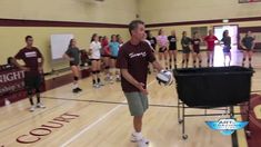 a man holding a volleyball ball on top of a hard wood floor in a gym