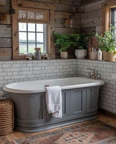 a bath tub sitting next to a window with plants on the wall and rug in front of it