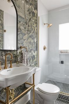 a white toilet sitting next to a sink in a bathroom under a mirror and gold faucet