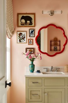 a bathroom with pink walls and pictures on the wall above the sink, along with a red mirror