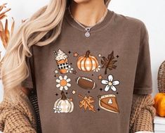 Experience the essence of autumn with our exclusive fall favorites shirt. This cozy and stylish tee showcases beloved seasonal elements, including delicious pumpkin pie, the thrill of football, and the vibrant colors of fall leaves. Perfect for those crisp days spent enjoying the outdoors or gathering with friends and family, this shirt lets you celebrate the season in comfort and style. Crafted from soft, breathable fabric, it provides an ideal fit for any occasion. Whether you're heading to a football game, enjoying a pumpkin-spiced latte, or taking a stroll through a kaleidoscope of fall colors, this shirt is a must-have addition to your wardrobe. Embrace the warmth and joy of fall--get yours today! Casual Brown T-shirt For Fall, Brown Graphic Print T-shirt For Fall, Relaxed Fit T-shirt For Fall, Brown Graphic Tee For Fall, Fall Graphic Tee In Brown, Trendy Brown T-shirt For Fall, Colors Of Fall, Friends Gathering, Delicious Pumpkin