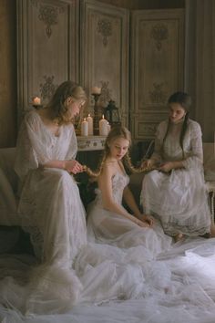 three women in white dresses are sitting on a couch and one is wearing a wedding dress