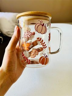 a hand holding a glass mug with fall decorations on it