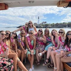 a group of women sitting on top of a boat in front of the ocean wearing sashs