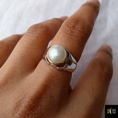 a close up of a person's hand wearing a ring with a pearl on it