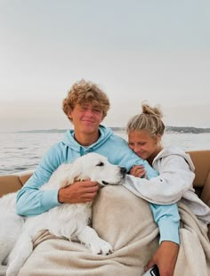 a man and woman are sitting on a boat with their dog, who is wrapped in a blanket