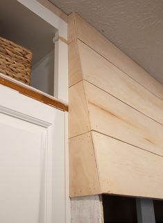 a basket sitting on top of a wooden shelf next to a white door in a room