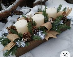 some white candles are sitting in a wooden box with pine cones and evergreen leaves on it