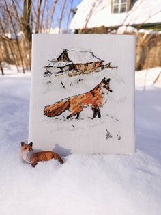 a needled picture of a fox in the snow next to a small figurine