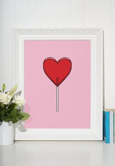 a red heart lollipop on a stick in front of a pink background with white flowers