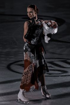 a female figure skating on an ice rink holding a bouquet of flowers in her hand