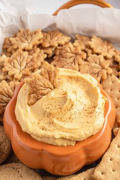 an orange bowl filled with hummus and crackers on top of a tray full of cookies