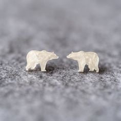 two small white bears standing next to each other on top of a gray surface,