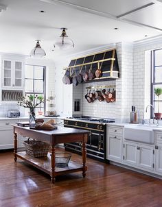 a kitchen with white cabinets and wooden floors, an island in the middle is surrounded by pots and pans