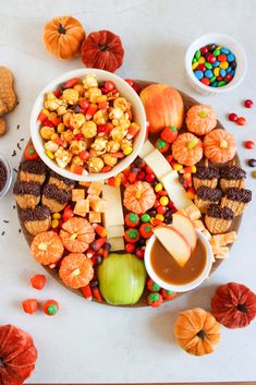 a platter filled with candy corn, candies and pumpkins next to other snacks