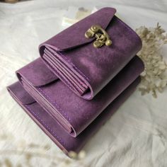 two purple purses sitting on top of a white bed next to a flower bouquet