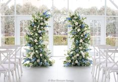 two white chairs with blue and white flowers on them in front of a large window