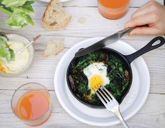 a person holding a fork over a skillet with an egg in it on a white plate