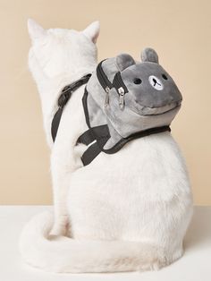 a cat with a backpack on it's back sitting next to a stuffed animal