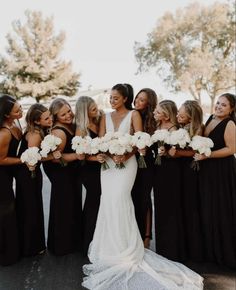 a group of women standing next to each other wearing black dresses and holding bouquets