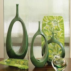 three green vases sitting on top of a wooden table next to a glass bowl