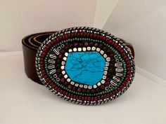 Pewter mosaic belt buckle measures 3.5 x 2.5 inches. An asymmetrical blue howlite cabochon, surrounded by silver cube beads and mahogany riverstone beads is flanked by silver accent beads and surrounded by; 1. A row of turquoise seed beads  2. A row of rust-colored beads 3. A row of seed beads alternating in rust, sky blue, white and silver. The mosaic buckle has a hook and a D-ring, which can attach to any snap-type belt strap of up to one and a half inches in width. This pewter buckle comes wi Turquoise Bohemian Belt With Concho, Handmade Bohemian Belt Buckles As Gift, Turquoise Bohemian Belt Buckle With Antique Detail, Handmade Western Belt Buckles As Gift, Handmade Western Belt Buckles For Gift, Blue Howlite, Statement Belt, Suspender Belt, Silver Accents