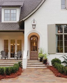 a white house with steps leading up to the front door and two chairs on the porch