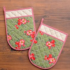 two oven mitts with flowers on them sitting on top of a wooden table next to each other