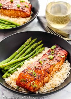 two pans with salmon and asparagus on top of white rice in front of a glass of wine