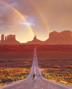 two rainbows in the sky over an empty road with mountains and desert behind it