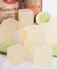 several cubes of ice next to a bottle of booze and lime wedges